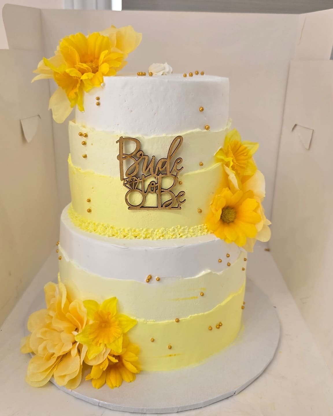 Two tier yellow and white Bride to Be cake with large yellow blooms and a gold script topper