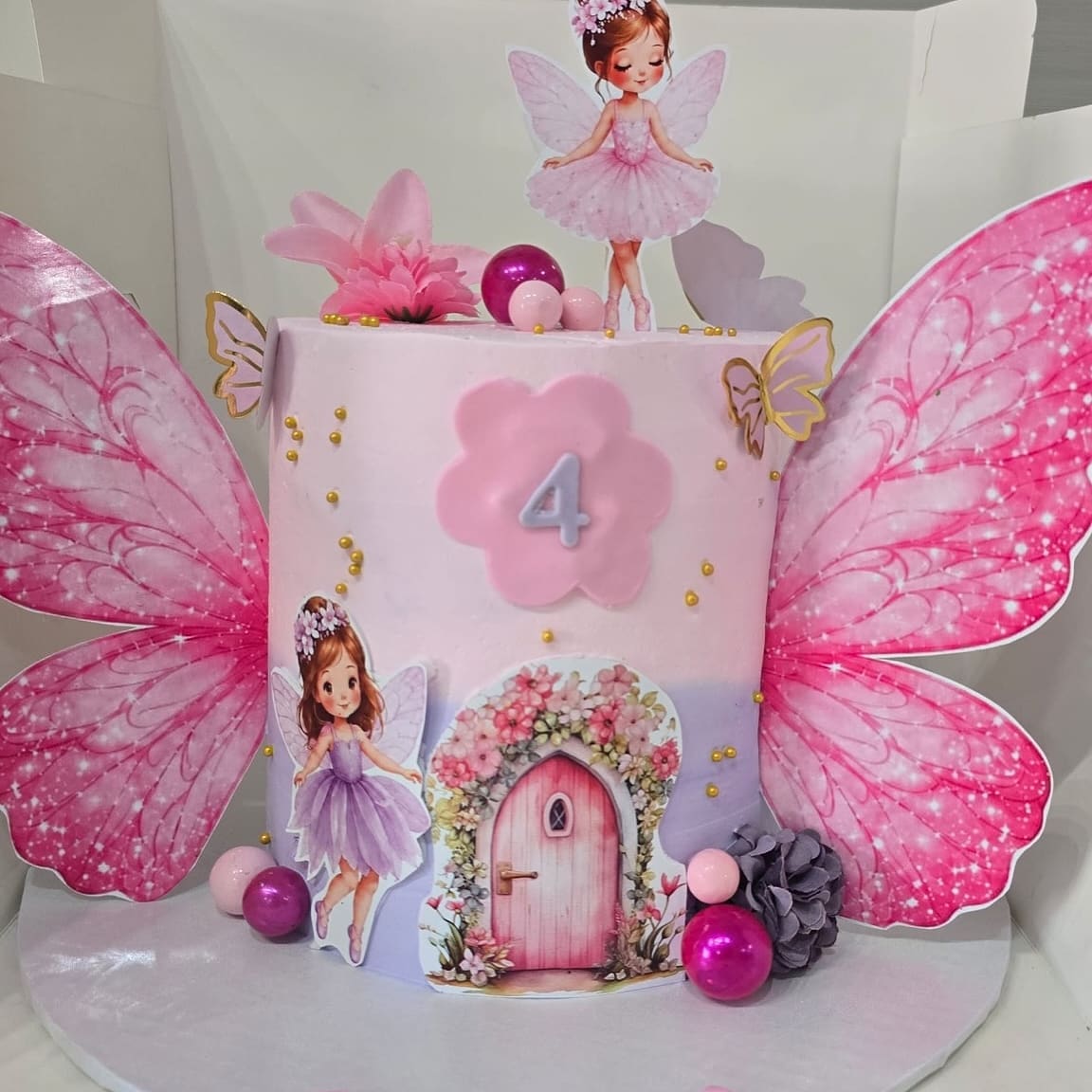 Fairy garden cake for a fourth birthday with pink butterfly wings, a fairy topper and a flower framed fairy door