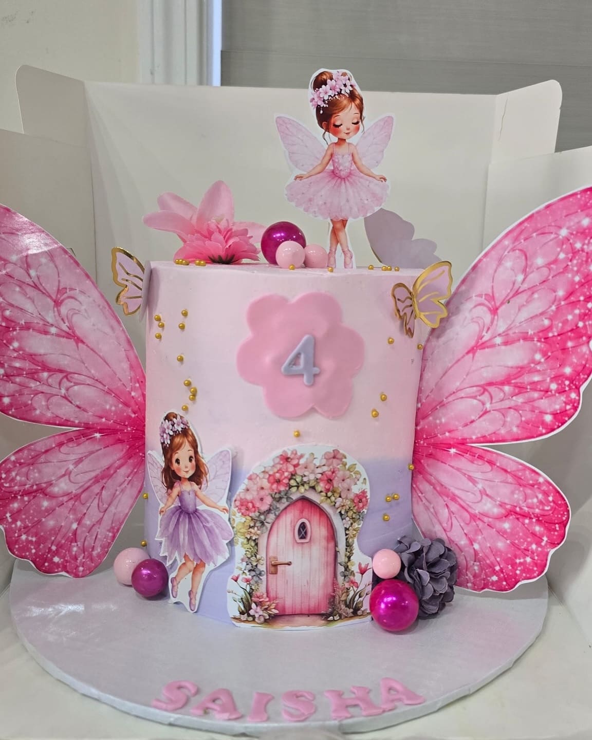 Fairy garden cake for a fourth birthday with pink butterfly wings, a fairy topper and a flower framed fairy door