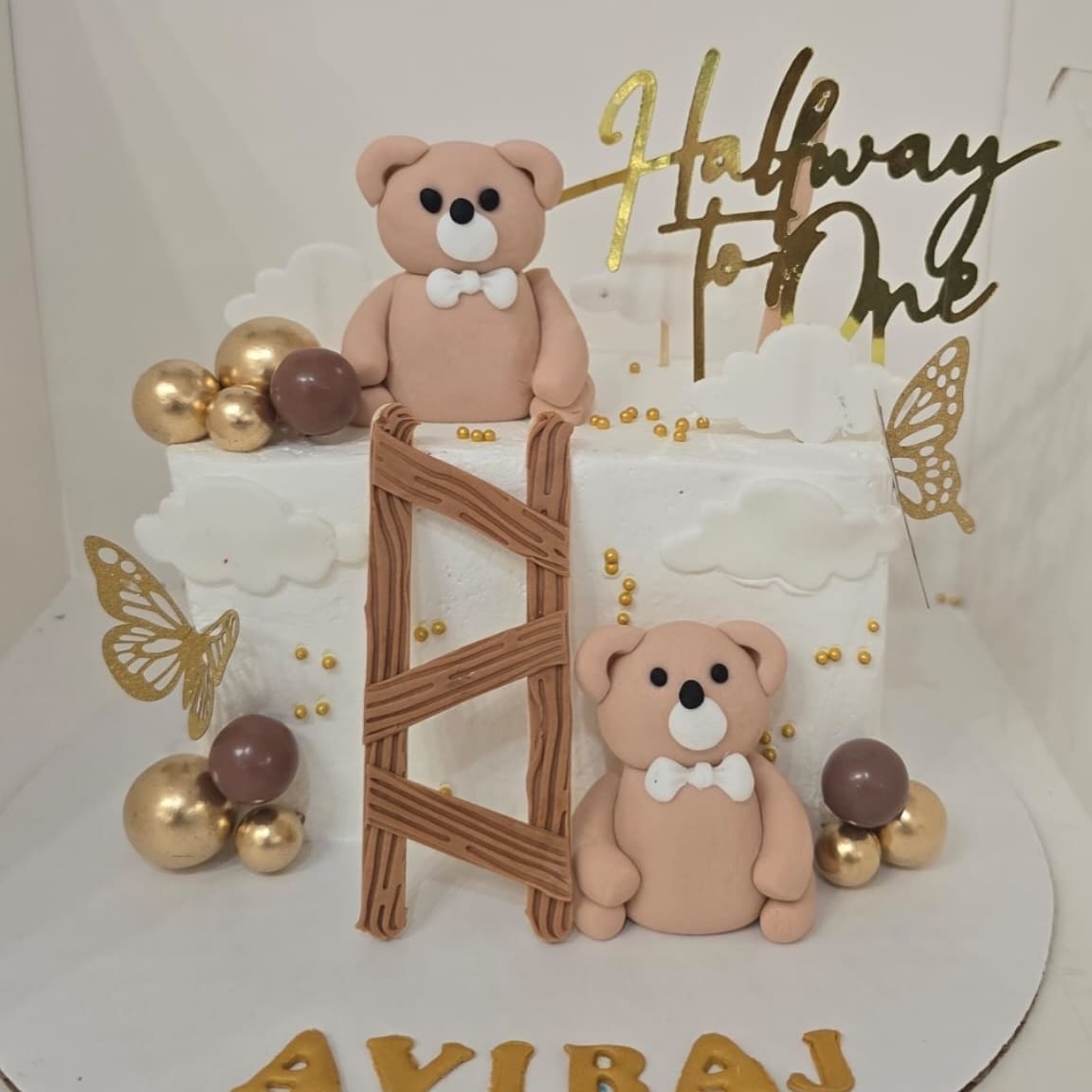 Half Way to One cake with two sugar teddy bears, a wooden style ladder, gold spheres and a gold script topper