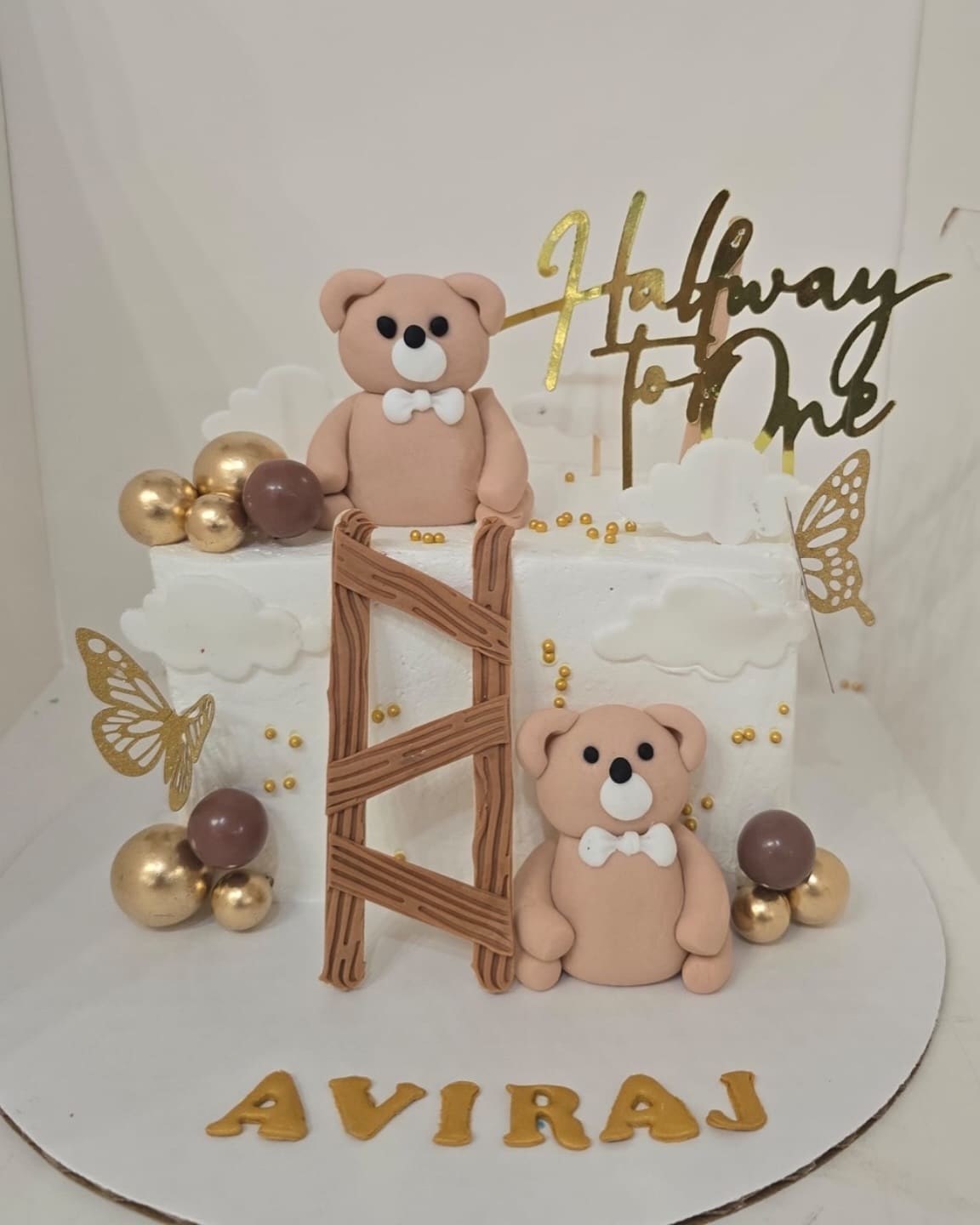 Half Way to One cake with two sugar teddy bears, a wooden style ladder, gold spheres and a gold script topper