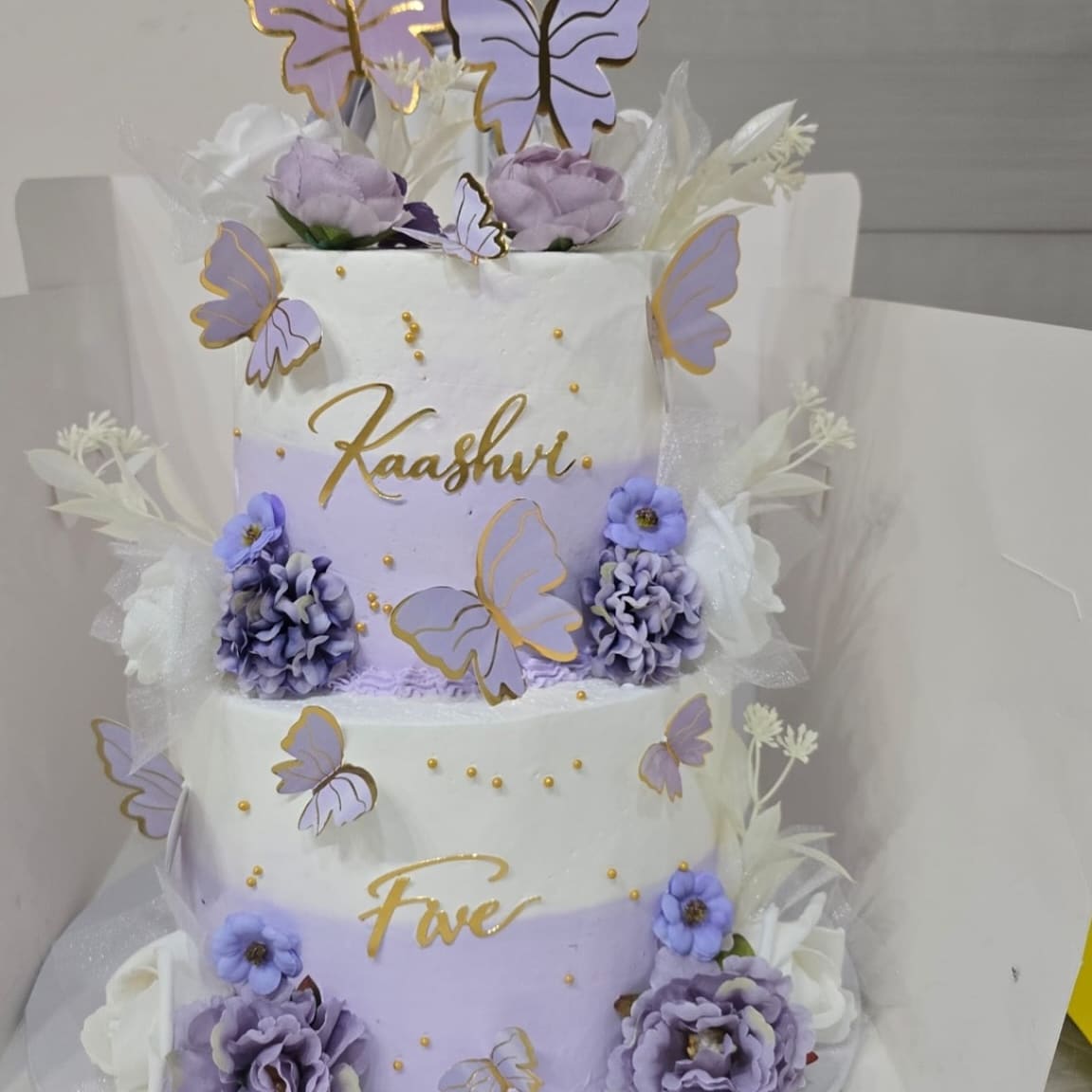 Two tier lilac birthday cake with purple roses, lilac butterfly toppers and gold lettering for a fifth birthday