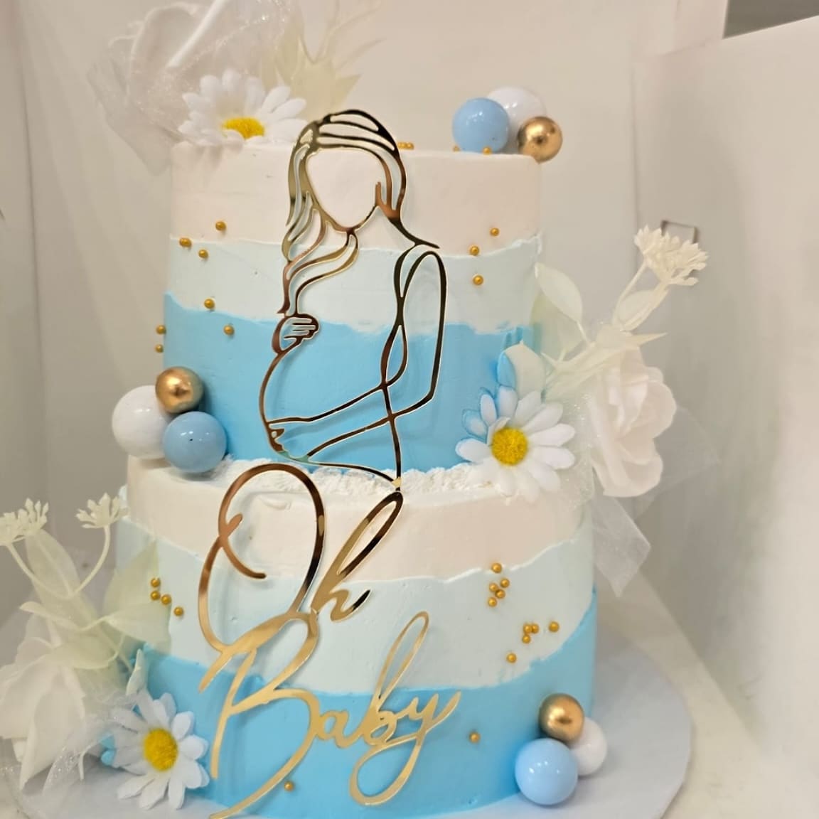 Oh Baby shower cake in soft blue and white with a gold line drawn silhouette topper and white daisies