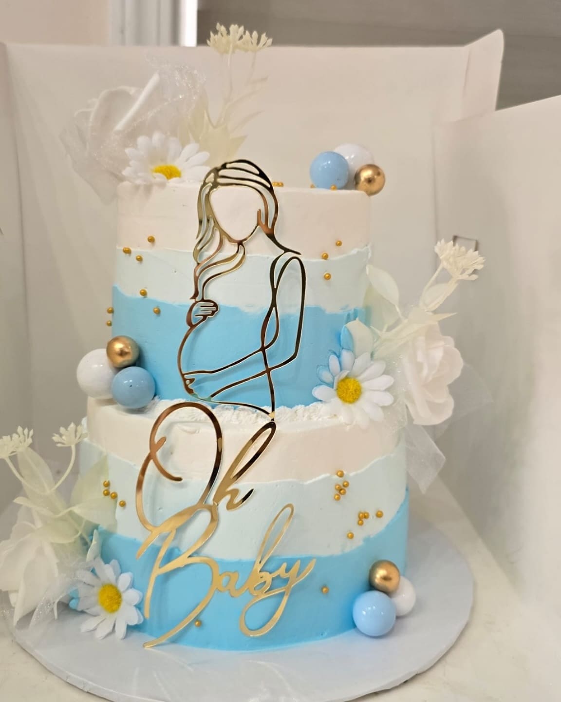 Oh Baby shower cake in soft blue and white with a gold line drawn silhouette topper and white daisies