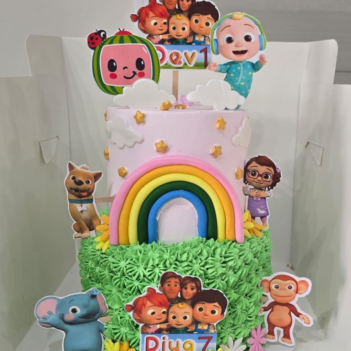 Cartoon themed seventh birthday cake with a sugar rainbow, character toppers and piped green grass