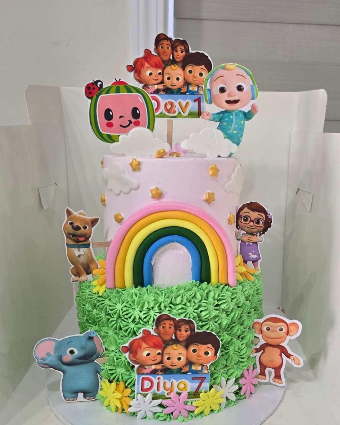 Cartoon themed seventh birthday cake with a sugar rainbow, character toppers and piped green grass