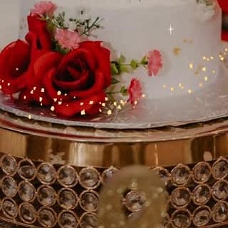 White wedding cake on a gold mirrored stand, dressed with deep red roses
