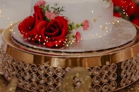White wedding cake on a gold mirrored stand, dressed with deep red roses