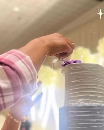 Hand placing a lilac flower on the top tier of a tall white wedding cake at the venue